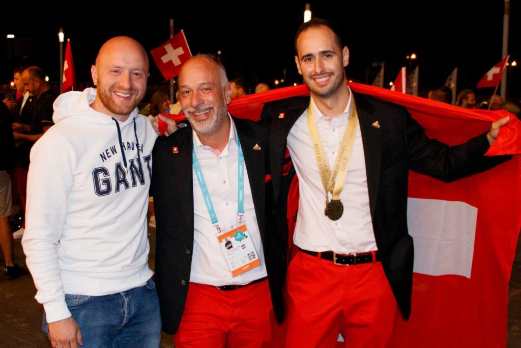 Giorgio Besomi ist Europameister 2023! Er posiert mit Trainier Minur Ajdaroski und Experte Ivan Fankhauser